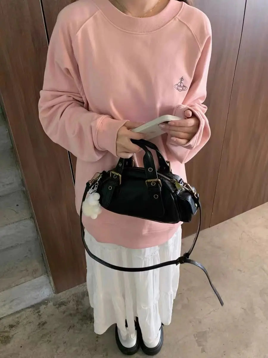 Person wearing a pink sweatshirt and white skirt holding a black handbag.