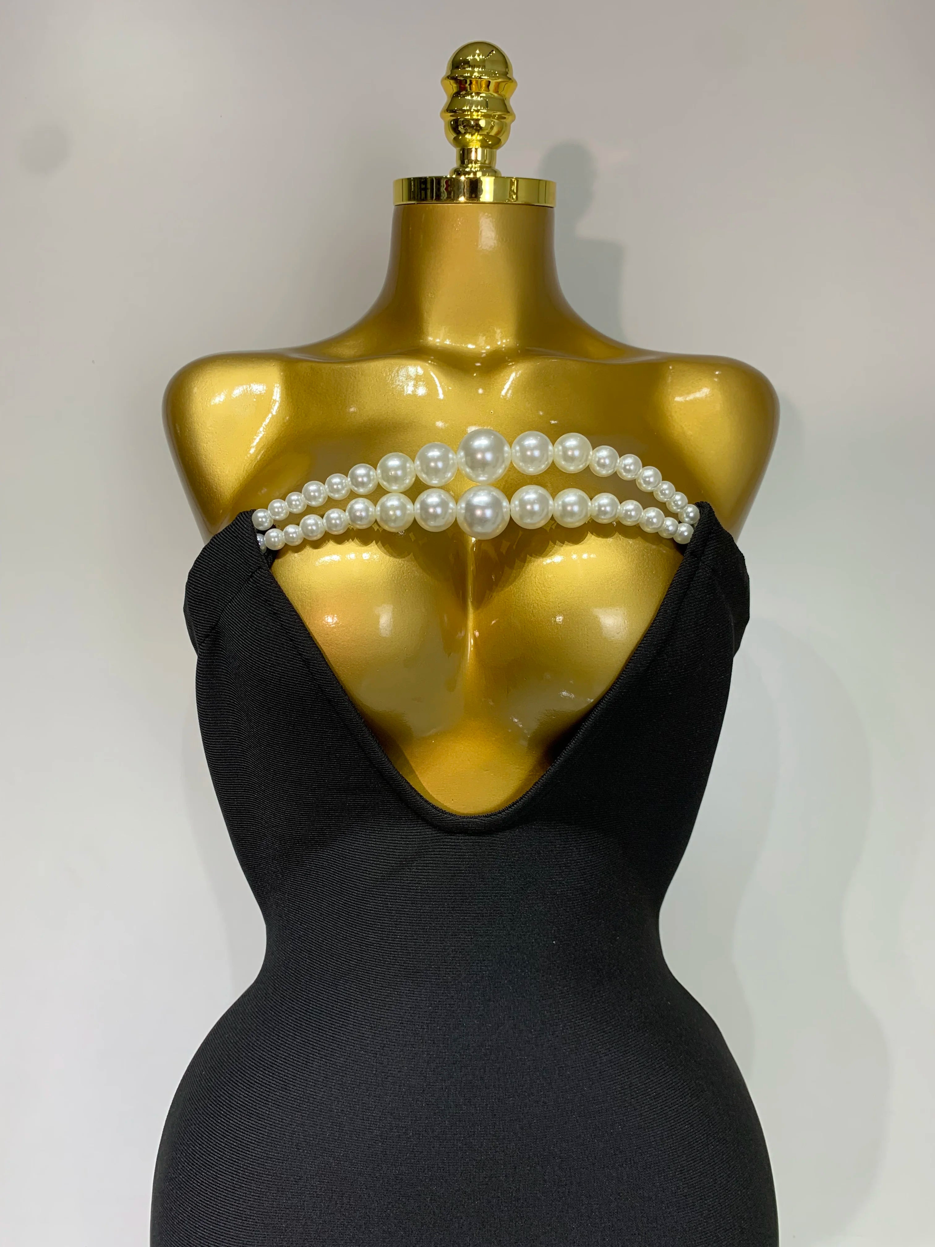 Black strapless dress with pearl embellishments on a gold mannequin against a white background