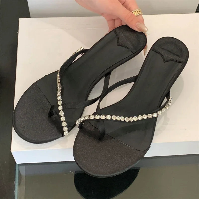 Black sandal with decorative straps held by a hand on a white surface.