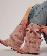 Ribbed knit slouchy boots with satin pointed toe and bow accent on a person's legs.