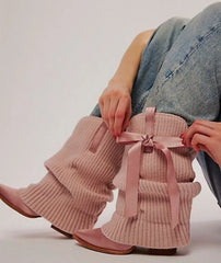 Ribbed knit slouchy boots with satin pointed toe and bow accent on a person's legs.