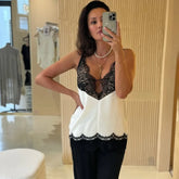 Woman taking a mirror selfie wearing a white and black lace top.