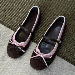 Pair of brown shoes with pink bows on a textured surface