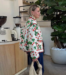 Person wearing a colorful quilted jacket in a kitchen setting with a plant and appliances.
