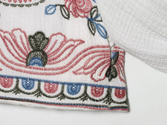 Detail of the sleeve cuff and fabric texture on the white embroidered blouse.