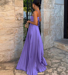 Woman in a purple dress standing against a stone wall.