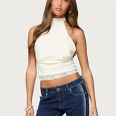 Woman wearing a white halter top with lace detail and blue jeans on a plain background