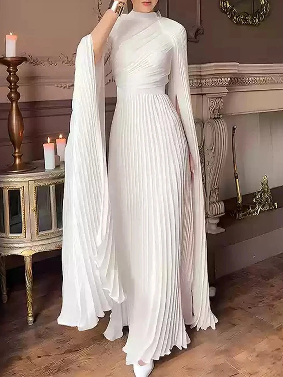 Woman wearing a white pleated dress in an elegant room with candles and decorative elements.
