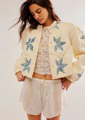 Woman wearing a cream-colored jacket with blue floral patterns, white lace top, and shorts on a light background