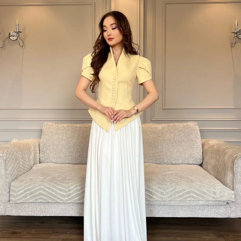 Woman in a yellow top and white skirt standing in a living room with a gray sofa.