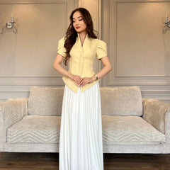 Woman in a yellow top and white skirt standing in a living room with a gray sofa.