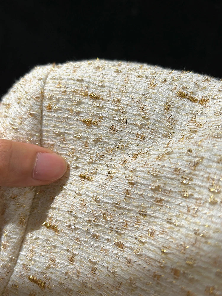 Close-up of textured fabric with gold specks and a finger for scale.