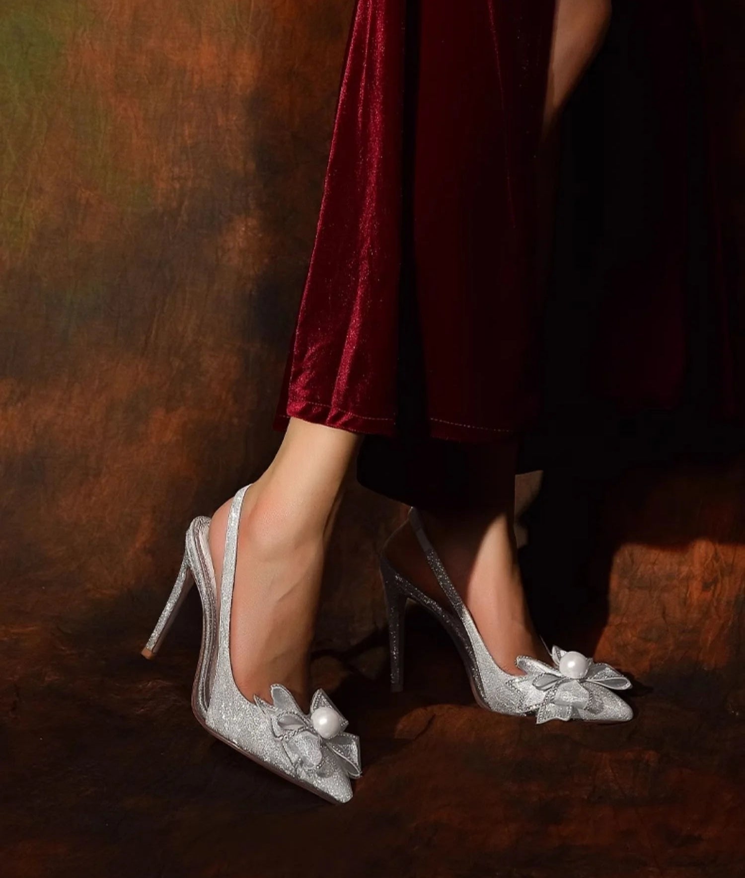 Silver high-heeled shoes with floral details on a dark background