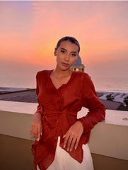 Woman in a red dress standing against a sunset sky with a building in the background.