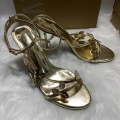 Gold high-heeled sandals on a white surface with a brown box in the background