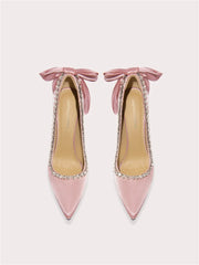 Pink high-heeled shoes with bow details and rhinestone embellishments on a light gray background