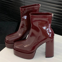 Pair of glossy burgundy platform boots on a white surface with a dark background