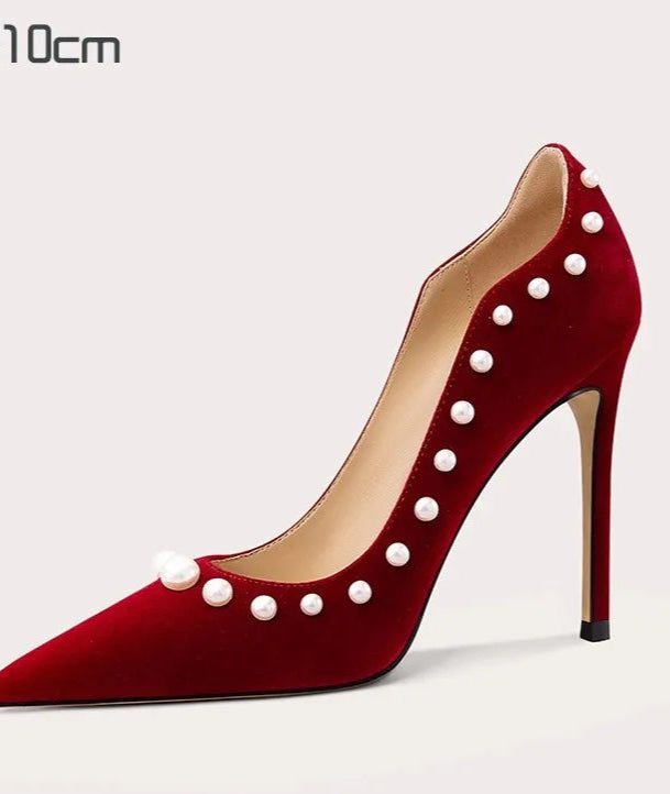 Red high-heeled shoe with pearl embellishments on a light gray background
