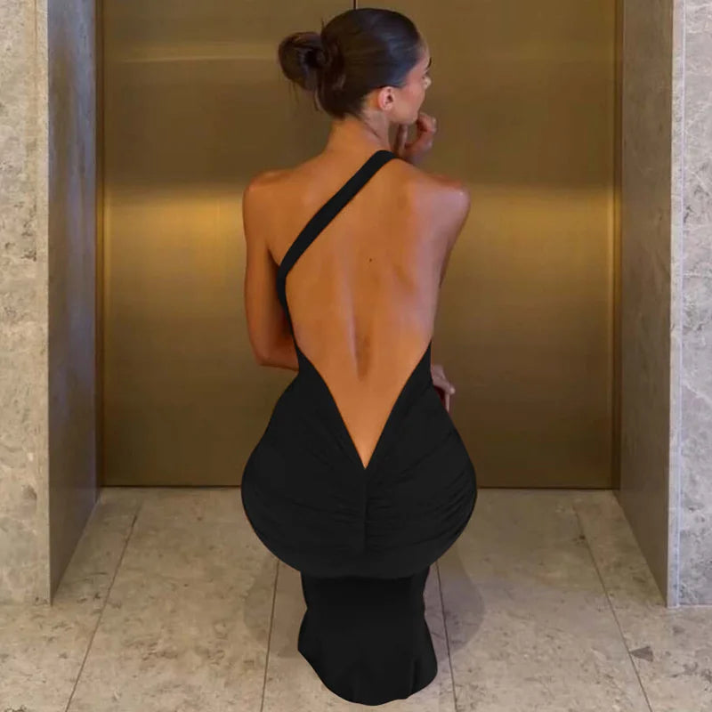 Woman in a black dress with an open back standing against a gold wall.