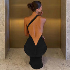 Woman in a black dress with an open back standing against a gold wall.