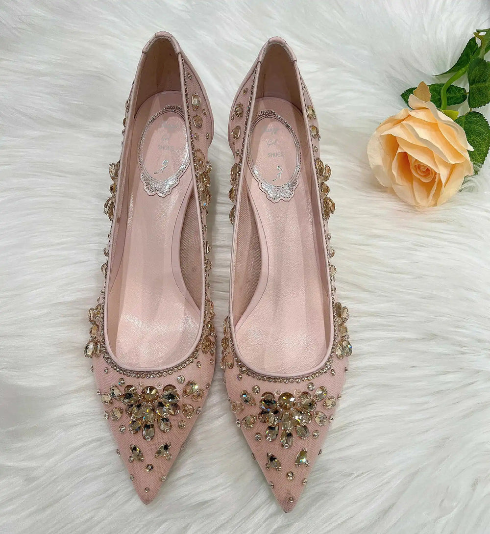 Pink high-heeled shoes with gold embellishments on a white surface with a peach rose.