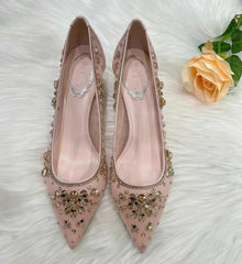 Pink high-heeled shoes with gold embellishments on a white surface with a peach rose.