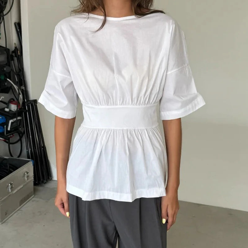 Person wearing a white blouse with a belt and gray pants in an indoor setting