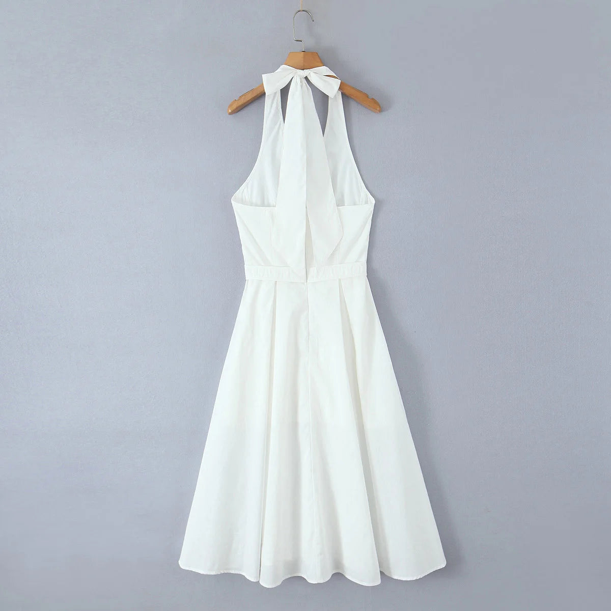 White halter neck dress on a wooden hanger against a gray background