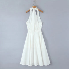 White halter neck dress on a wooden hanger against a gray background