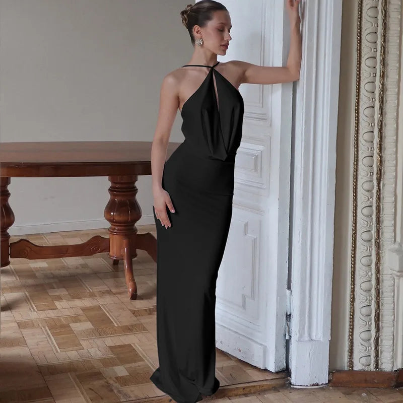 Woman in a black evening gown standing in an elegant room with wooden table and decorative wall.
