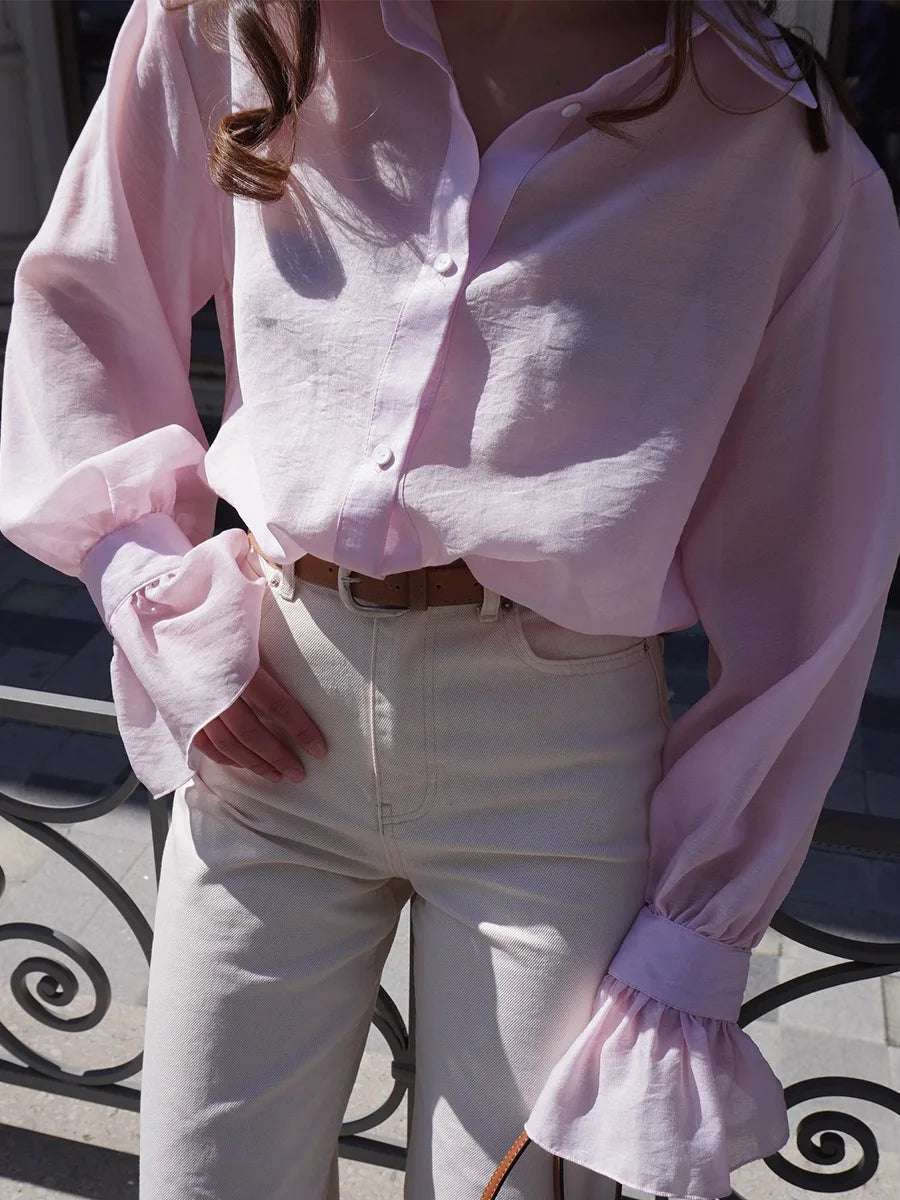 Person wearing a light pink blouse with long sleeves and white pants, standing on a patterned pavement.