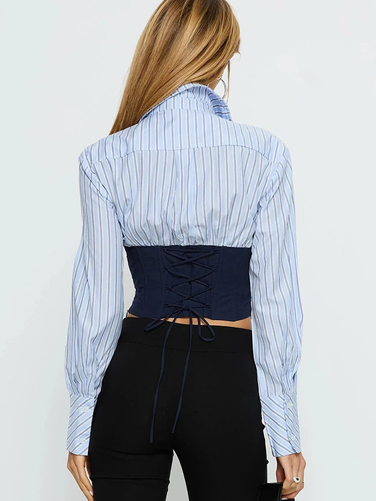 Person wearing a blue and white striped shirt with a black corset-style top underneath on a plain background