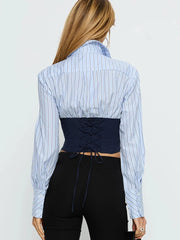 Person wearing a blue and white striped shirt with a black corset-style top underneath on a plain background