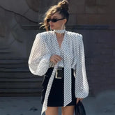 Woman wearing a polka dot blouse and black skirt against a textured wall.