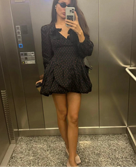 Person taking a mirror selfie wearing a black polka dot dress in an elevator.