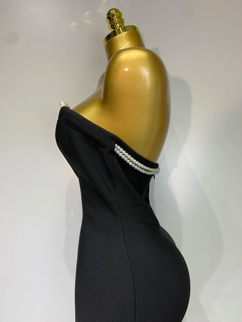 Black dress with pearl details on a gold mannequin against a white background