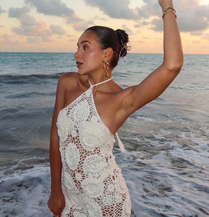 Woman in a white lace dress standing on a beach with sunset in the background