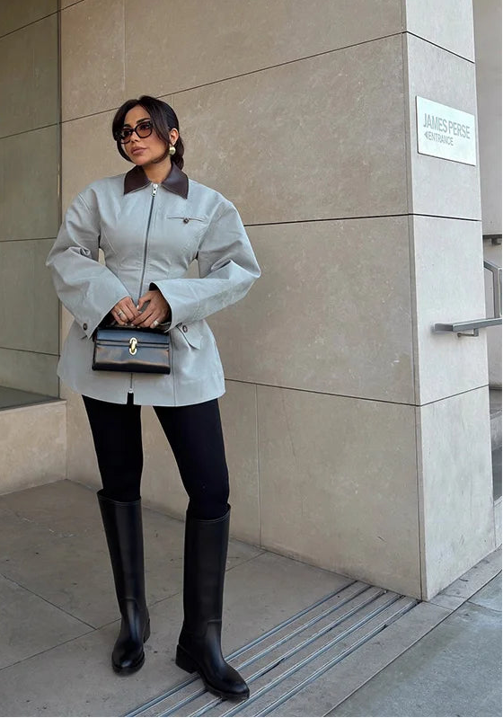 Woman in a gray coat and black knee-high boots standing in front of a building with 'TO WEST' sign.