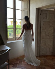 Woman in a white dress standing by an open window with a view of greenery.