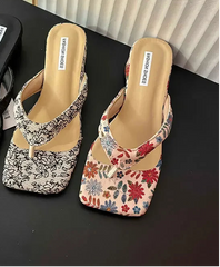Three pairs of floral and plain sandals on a black surface with a blurred magazine in the background.