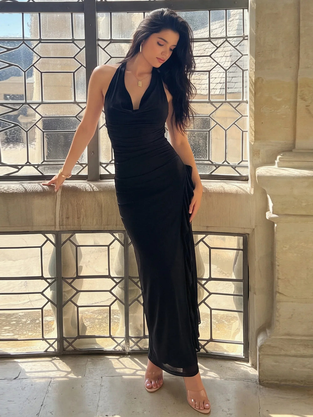 Model leaning on a window frame wearing a black ruffled halter neck maxi dress