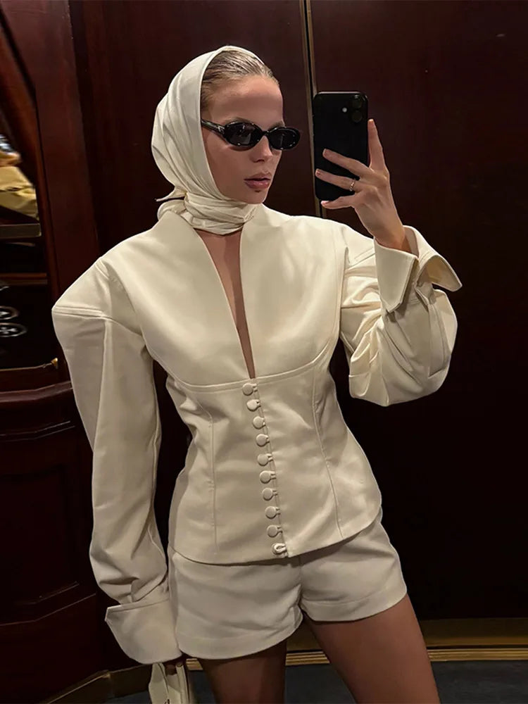 Person wearing a white outfit with a deep neckline and button details, standing in front of a mirror.