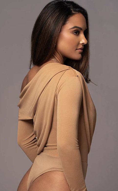 Woman wearing a beige bodysuit against a gray background