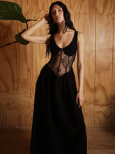 Woman wearing a black lace dress against a wooden wall.
