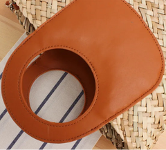Brown leather strap on a woven bag with striped fabric underneath