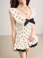Woman wearing a polka dot dress with a black bow and pearl necklace on a plain background