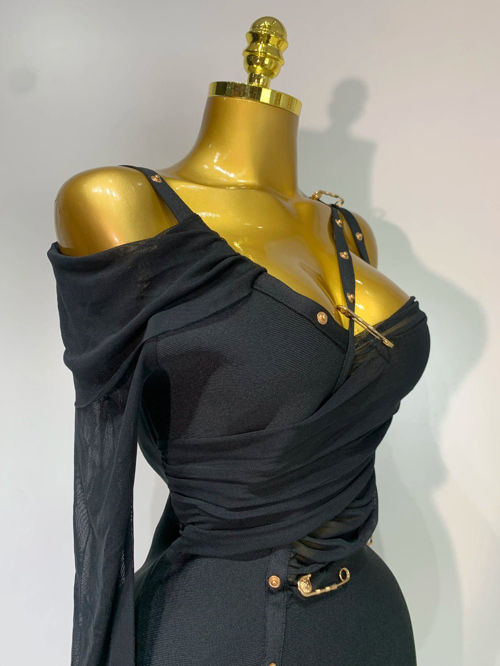 Black off-shoulder top on a gold mannequin against a white background