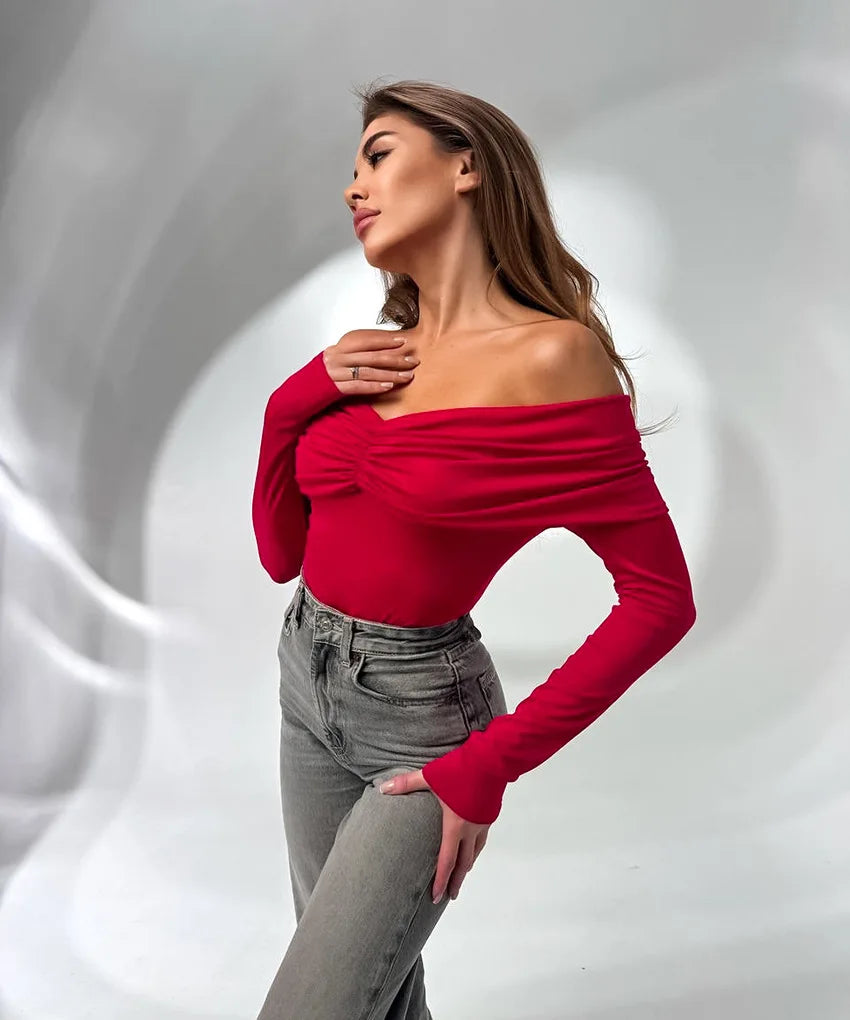 Woman wearing a red off-shoulder top and gray pants against a white background