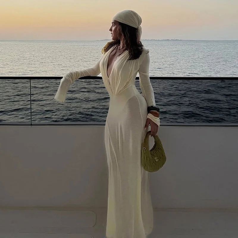 Woman in a white dress standing on a boat with a scenic ocean view.