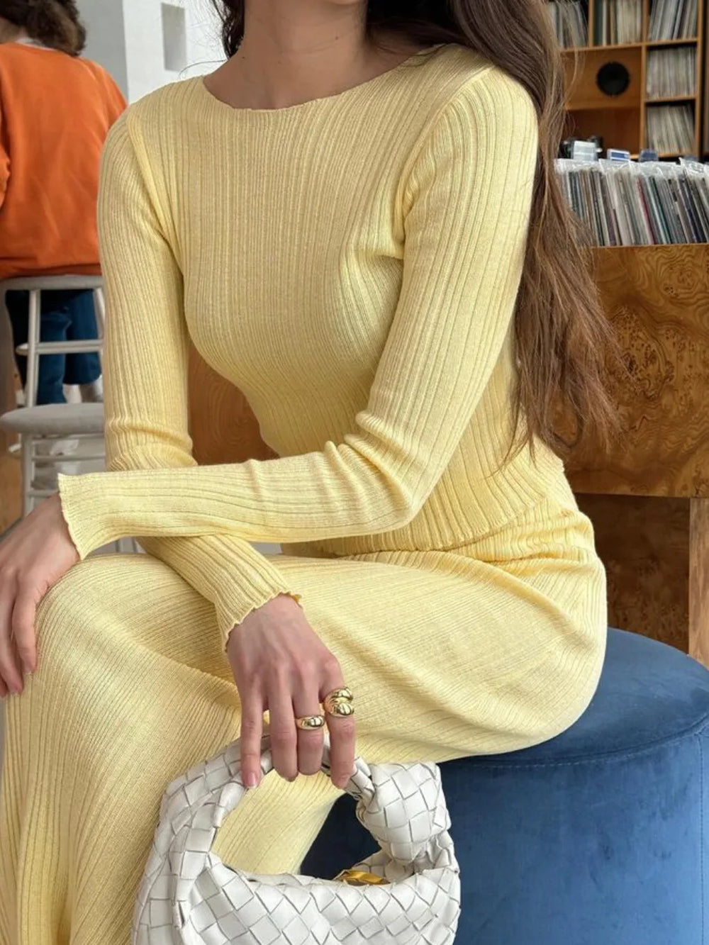 Person wearing a yellow ribbed sweater sitting on a blue chair.